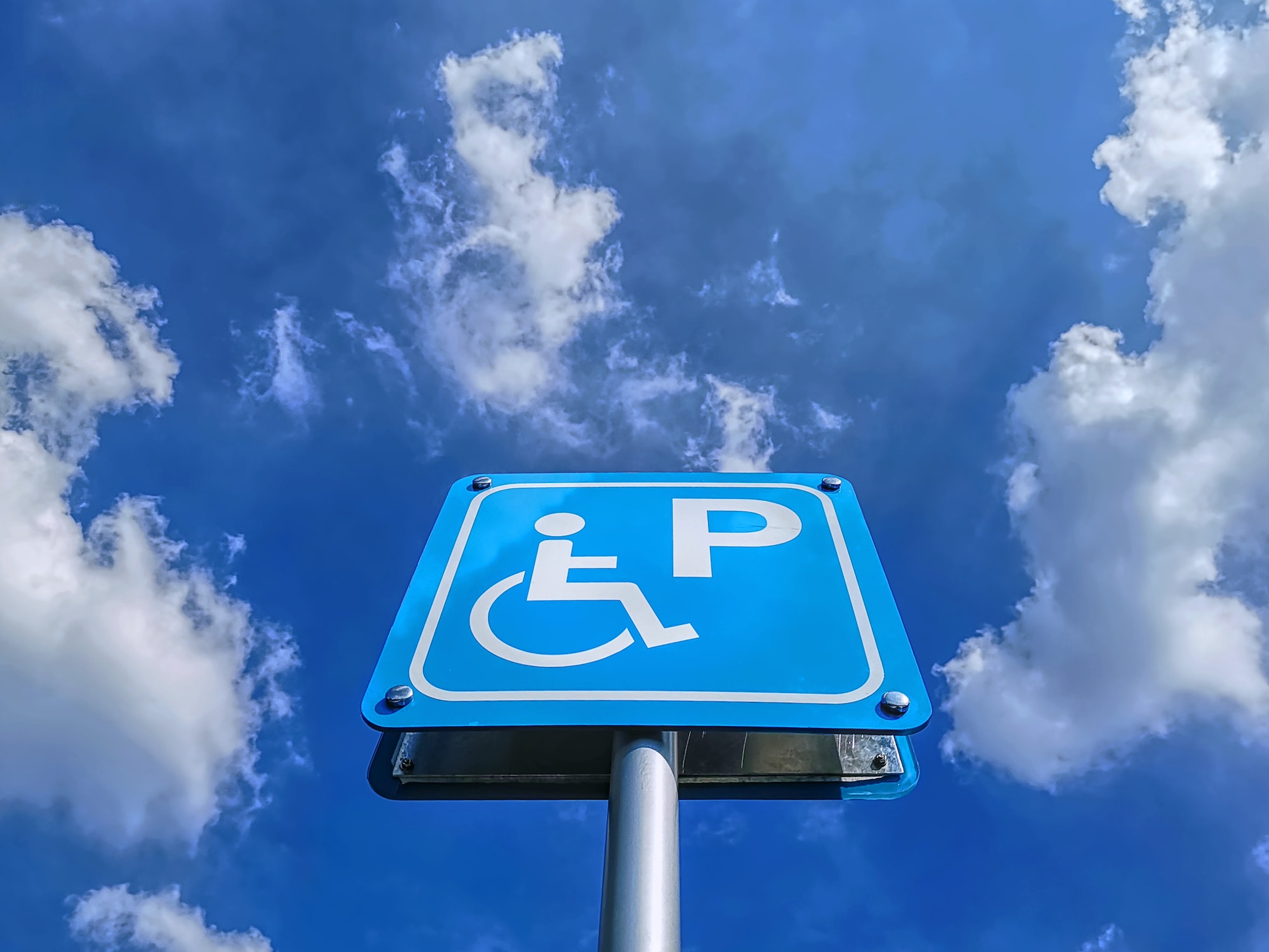 Low Angle View of Blue Handicapped Parking Sign Against Blue Cloudy Sky at Day Time